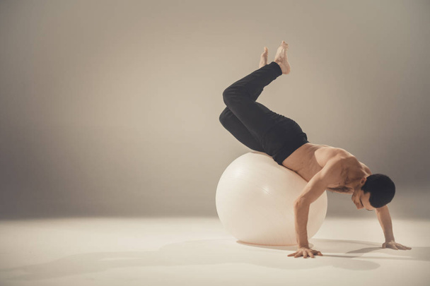 young man dancer making exercises and posing with yoga ball in studio - Foto, Imagen