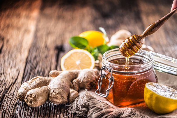 Honey jar dipper ginger lemon and mint herbs on wooden table. - 写真・画像