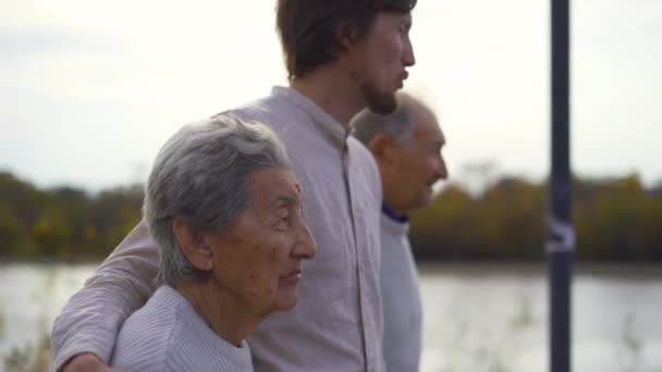 Slowmotion shot of a young man walking with his grandparents on a walkway along a riverside - Footage, Video
