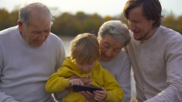 La toma en cámara lenta del nieto junto con su padre enseñan a sus abuelos cómo usar aplicaciones en su teléfono celular
 - Imágenes, Vídeo