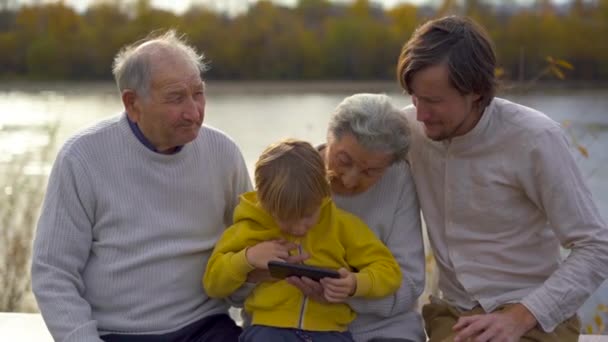Slowmotion shot of grandgrandson along with his father teach his grandgrand parents how to use applications on his cellphone - Footage, Video