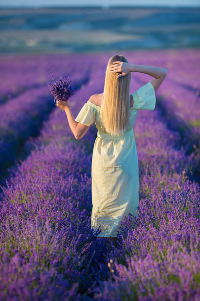 Smiling beautiful blond lady model on lavender field enjoy summer day wearing airy whit dress with bouquet of flowers - Zdjęcie, obraz