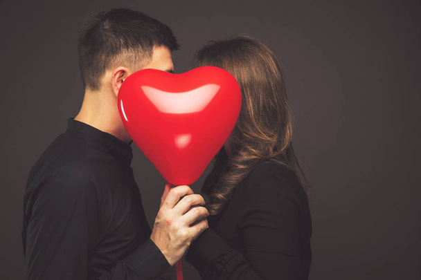 young couple with heart shaped red balloons near grey wall - Фото, изображение