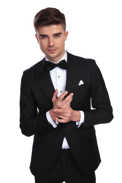 portrait of young man in black tuxedo holding palms together while standing on white background - Foto, Imagen