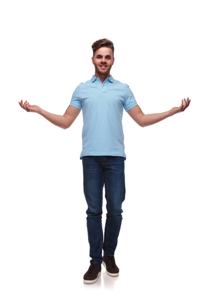 attractive man in polo shirt making a welcoming gesture with hands while stepping forward on white background, full length picture - Photo, Image