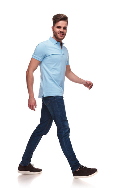 side view of joyful and handsome casual man wearing a blue polo shirt stepping on white background, full body picture - Photo, image