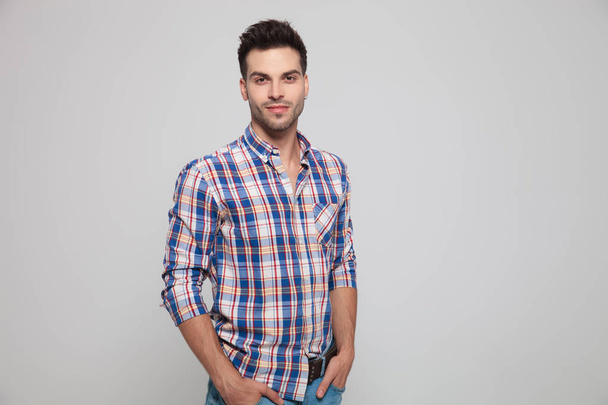 retrato de homem casual atraente vestindo uma camisa xadrez de pé com as mãos nos bolsos; fundo cinza claro
 - Foto, Imagem