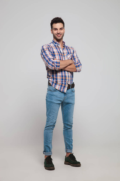 confident casual man wearing a shirt with checkers standing with arms folded on light grey background, full body picture - Foto, Imagem
