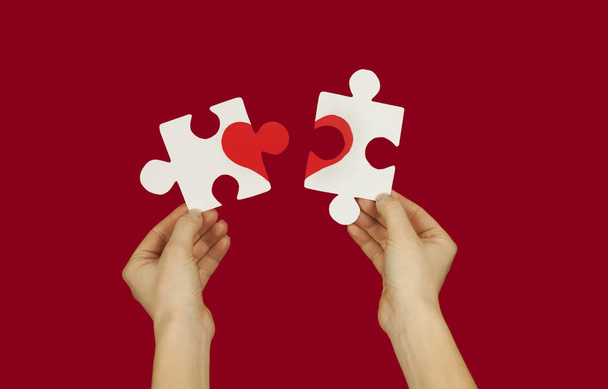Puzzle with a red heart in the hands of a loving couple. Valentine's day concept.On a red isolated background - Fotó, kép