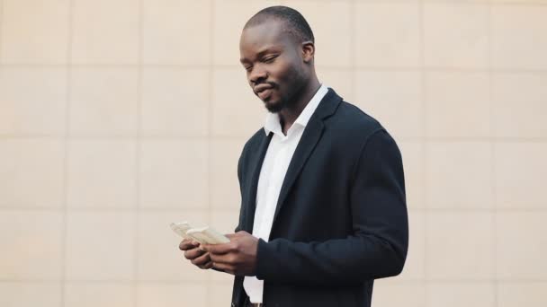 The young successful African American businessman is standing in the street and counting the money. Successful business, winnings, lottery, easy money concept - Filmati, video