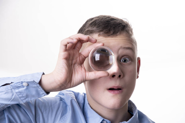 menino segura uma bola de vidro na frente de seu olho e você vê seu olho ampliado
 - Foto, Imagem