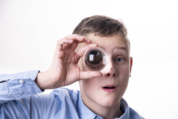 boy holds a glass ball in front of his eye and you see his eye enlarged - Photo, Image