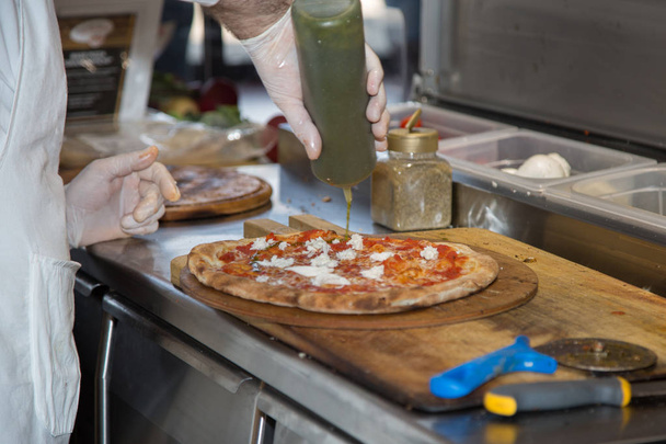 Pizza Maker que prepara una deliciosa pizza con queso Mozzarella, aceite y tomates
. - Foto, imagen