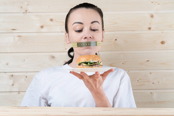 Ernährung. Porträt Frau will einen Burger essen, steckt aber im Mund fest, das Konzept der Ernährung, Junk Food, Willenskraft in der Ernährung - Foto, Bild