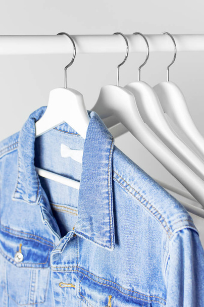 Blue denim jacket on white wooden coat hanger on a rod against light gray wall flat lay copy space. Denim, fashionable jacket, women's or men's trend clothing, fashion background. Store concept, sale - Photo, Image
