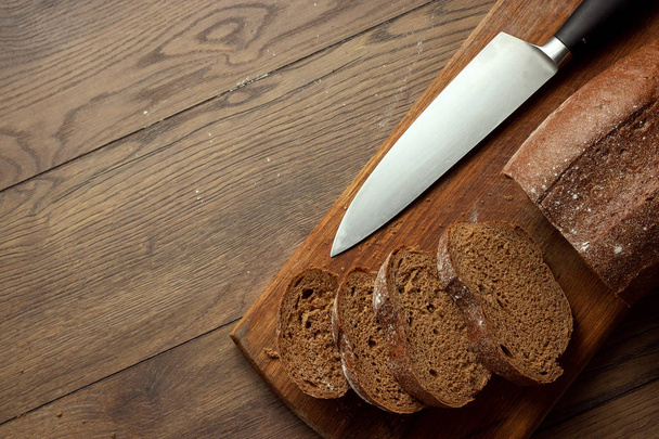 Creative background, sliced rye bread and a knife close-up, on a wooden cutting board, flat lay, copy space. The concept of fresh pastry, black bread. - Foto, Bild