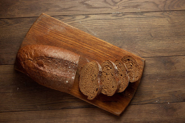 Creative background, freshly baked sliced rye bread on a wooden cutting board, flat lay, copy space. The concept of fresh pastry, black bread. - Photo, Image