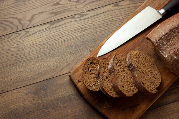 Creative background, sliced rye bread and a knife close-up, on a wooden cutting board, flat lay, copy space. The concept of fresh pastry, black bread. - Foto, Bild