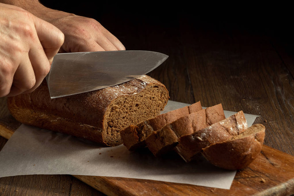 Creative background, male hands cut rye bread close-up, on a wooden cutting board, flat lay, copy space. The concept of fresh pastry, black bread. - Foto, immagini
