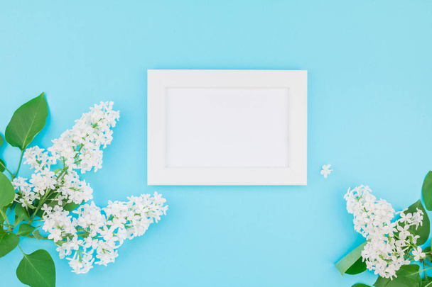 Creative flat lay concept top view of blank postcard frame mock up and white lilac flowers petals on pastel blue background with copy space in minimal style, template for lettering, text or design - Photo, Image