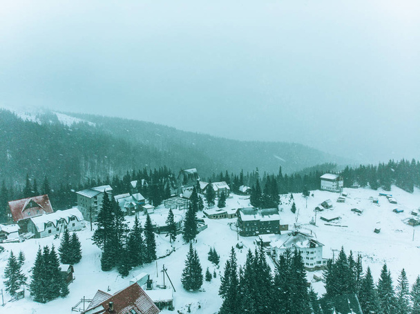вид с воздуха на маленькую деревню в заснеженных горах. пасмурная погода. снежная буря
 - Фото, изображение