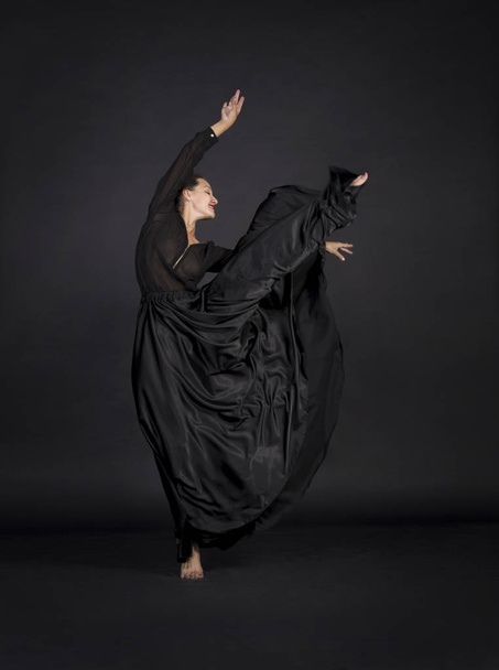 A young,smiling girl in black suit dancing modern choreography.Studio shot on dark background, isolated image. - Фото, изображение