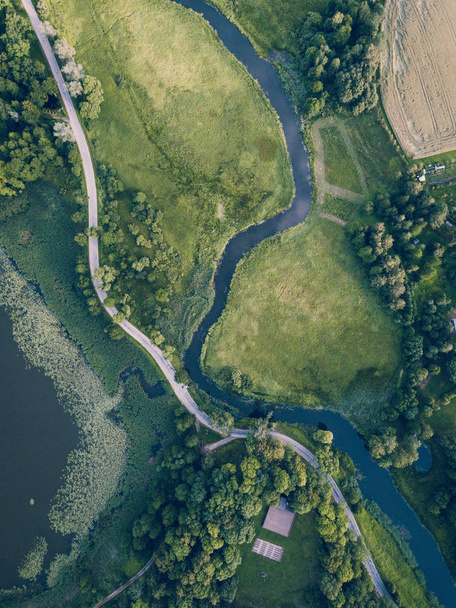 Foto aérea del camino que pasa por el río bajo los árboles, vista de arriba hacia abajo a principios de primavera en el día soleado - Concepto de vida pacífica en el campo en armonía, aspecto de película vintage
 - Foto, imagen