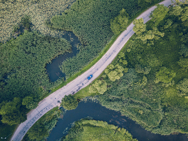 Foto aérea de un automóvil conduciendo por el camino que pasa por el río bajo los árboles, vista de arriba hacia abajo - Concepto de vida pacífica en el campo en armonía y viajes, libertad, aspecto de película vintage
 - Foto, imagen