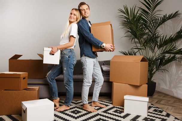 Image of young couple standing among cardboard boxes i - Фото, изображение
