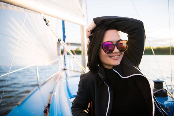 若い笑顔の黒髪女性サングラス晴れた秋の日のボートのボードの上に座って、川や海の上を歩く - 写真・画像