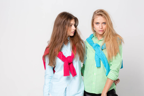 happy girlfriends women in shirts and a sweater on his shoulders. Fashion spring image of two sisters. Colorful colors clothes. Models with Blonde and light brown hair. Looking at camera . - Photo, Image