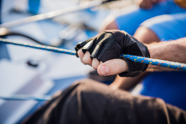 Nahaufnahme von Seefahrerwinden um ein Seil mittels Handgriff zum Aufwickeln. Er arbeitet mit beiden Händen. junger Mann steht auf Jacht. er ist stark - Foto, Bild
