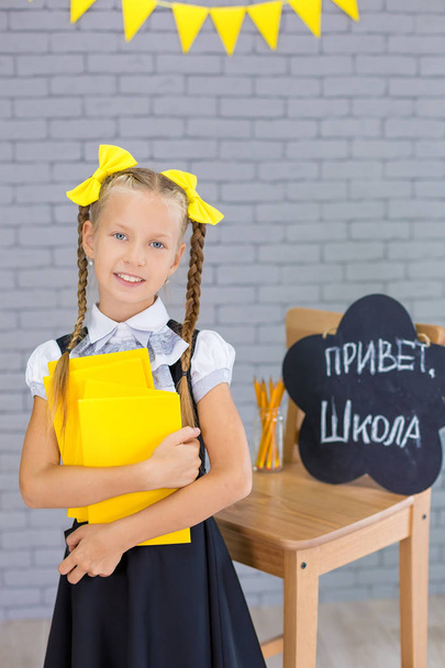 The schoolgirl in school uniform with books and textbooks is on a light gray background. Back to school. The new school year. Child education concept - Valokuva, kuva