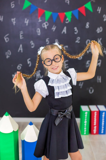 The schoolgirl in school uniform with books and textbooks is on a light gray background. Back to school. The new school year. Child education concept - Zdjęcie, obraz