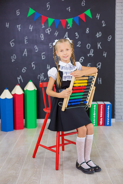 The schoolgirl in school uniform with books and textbooks is on a light gray background. Back to school. The new school year. Child education concept - Фото, изображение