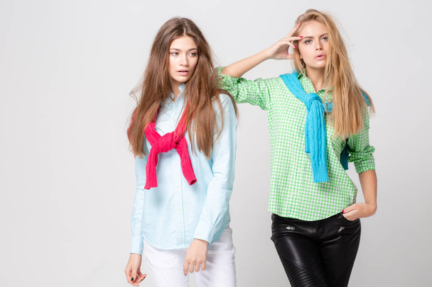 happy girlfriends women in shirts and a sweater on his shoulders. Fashion spring image of two sisters. Colorful colors clothes. Models with Blonde and light brown hair. Looking at camera and smiling. - Photo, Image
