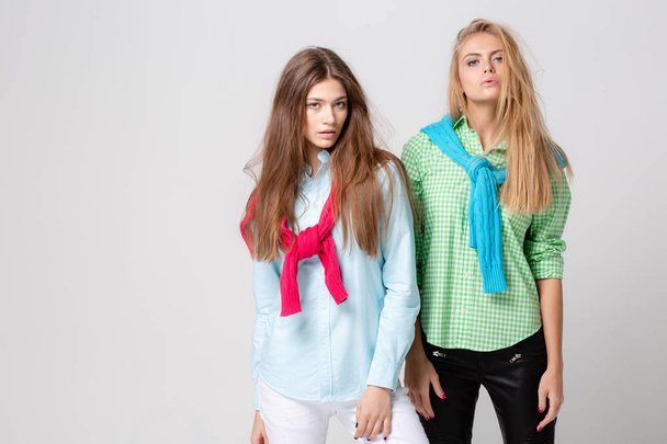 happy girlfriends women in shirts and a sweater on his shoulders. Fashion spring image of two sisters. Colorful colors clothes. Models with Blonde and light brown hair. - Photo, Image