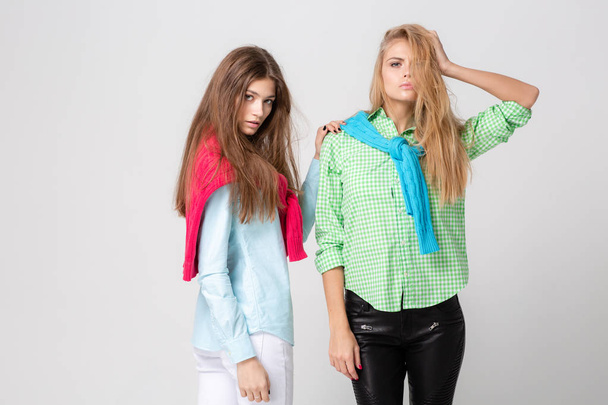 happy girlfriends women in shirts and a sweater on his shoulders. Fashion spring image of two sisters. Colorful colors clothes. Models with Blonde and light brown hair. - Photo, Image