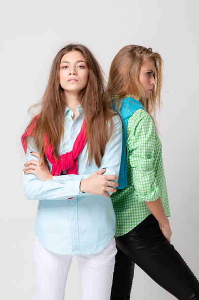 happy girlfriends women in shirts and a sweater on his shoulders. Fashion spring image of two sisters. Colorful colors clothes. Models with Blonde and light brown hair. Looking at camera and smiling. - 写真・画像