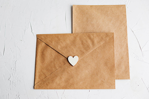 Top view of a letter to a beloved person. Kraft paper envelope, wooden small hearts and a shift of paper on white table. - Φωτογραφία, εικόνα