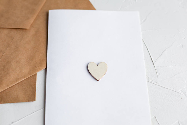 Top view of a letter to a beloved person. Kraft paper envelope, wooden small hearts and a shift of paper on white table. - Фото, зображення