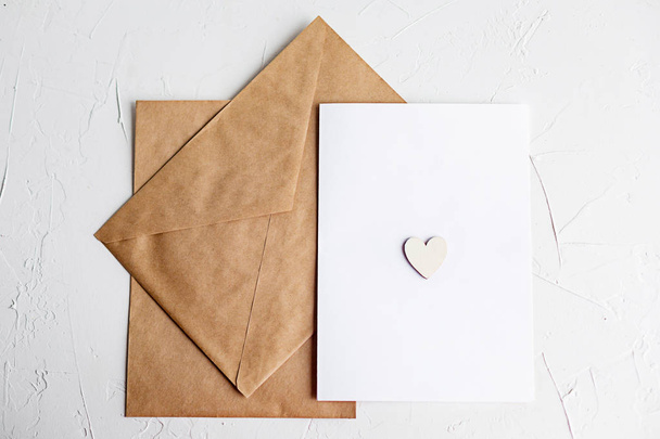 Top view of a letter to a beloved person. Kraft paper envelope, wooden small hearts and a shift of paper on white table. - Valokuva, kuva