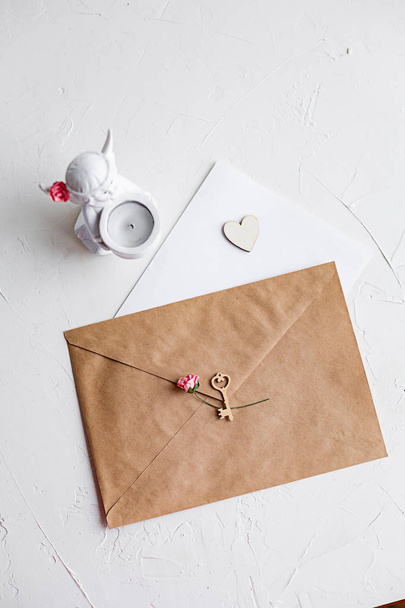 Top view of a letter to a beloved person. Kraft paper envelope, wooden small hearts and a shift of paper on white table. - Foto, immagini