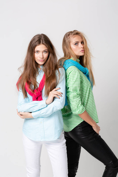 happy girlfriends women in shirts and a sweater on his shoulders. Fashion spring image of two sisters. Colorful colors clothes. Models with Blonde and light brown hair. Looking at camera and smiling. - Photo, Image