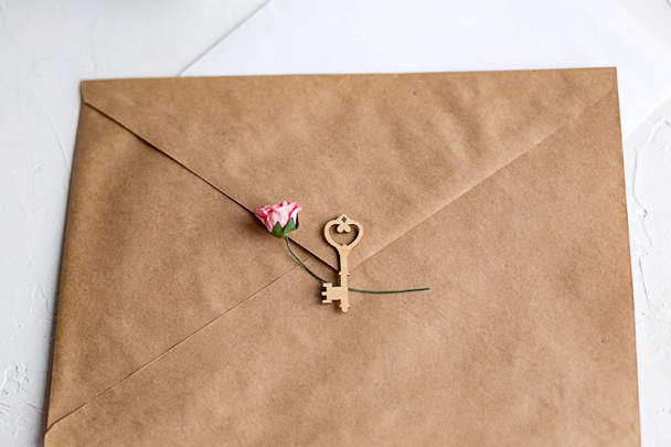 Top view of a letter to a beloved person. Kraft paper envelope, wooden small hearts and a shift of paper on white table. - Fotoğraf, Görsel