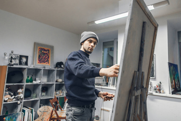 Young artist paints oil painting on canvas on the background of a cozy studio. Student artist works in art studio. Painting Concept. - Photo, Image