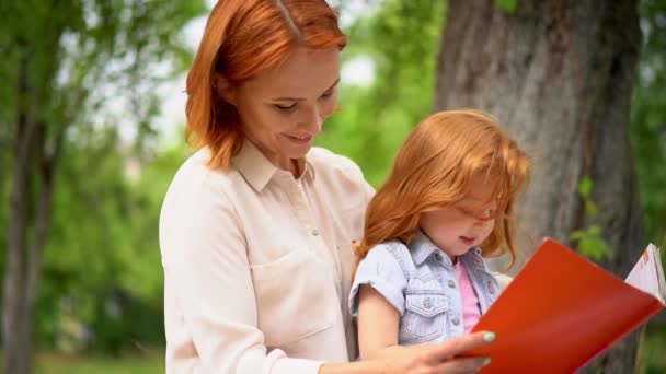 Mother and girl sit under a tree reading a book - Footage, Video
