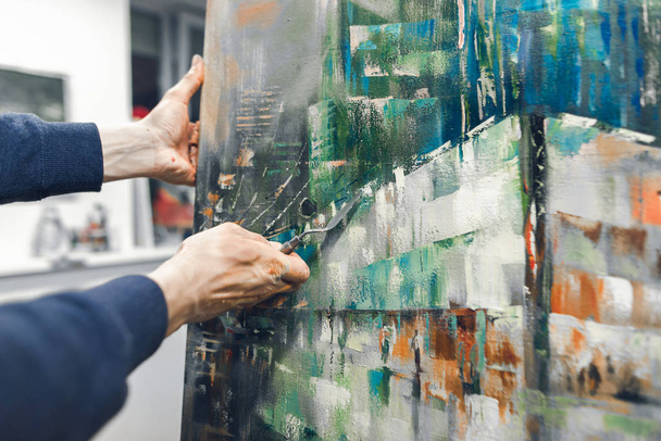 Artist with a knife palette in his hands draws a picture.Artist's hand with a knife palette paints on the canvas and a place for the text.Creation of picturesque paintings. Painting Concept.Copyspace - 写真・画像