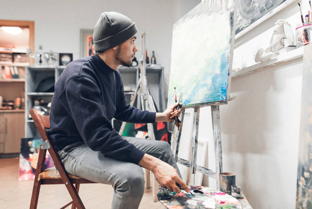 Portret van een student van de kunstenaar in de klas zit en schilderen van een schilderij op doek. Onderwijs aan art school. Man leert schilderen. - Foto, afbeelding