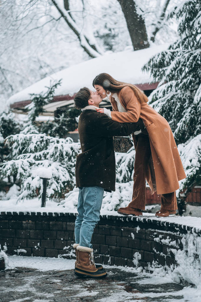 young guy and beautiful girl kiss in a snowy park - Photo, Image